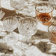 A variety of crystal glassware on a marble surface, including coupe glasses, tumblers, and highballs, illustrating the elegance and function of different drink-specific glasses.